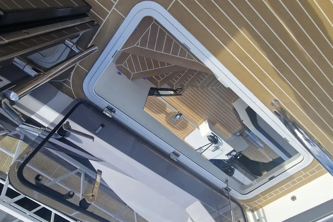View from above of a staircase on a luxury yacht with wooden flooring and metal railings, showcasing modern design elements.